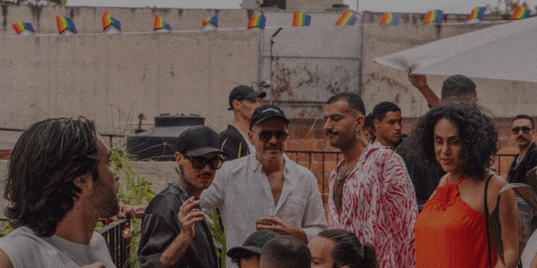 A lively group of people celebrating Mexico City Gay Pride 2024, standing around a table with colorful umbrellas.