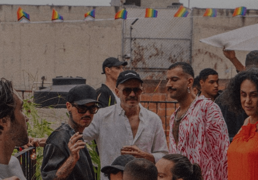 A lively group of people celebrating Mexico City Gay Pride 2024, standing around a table with colorful umbrellas.